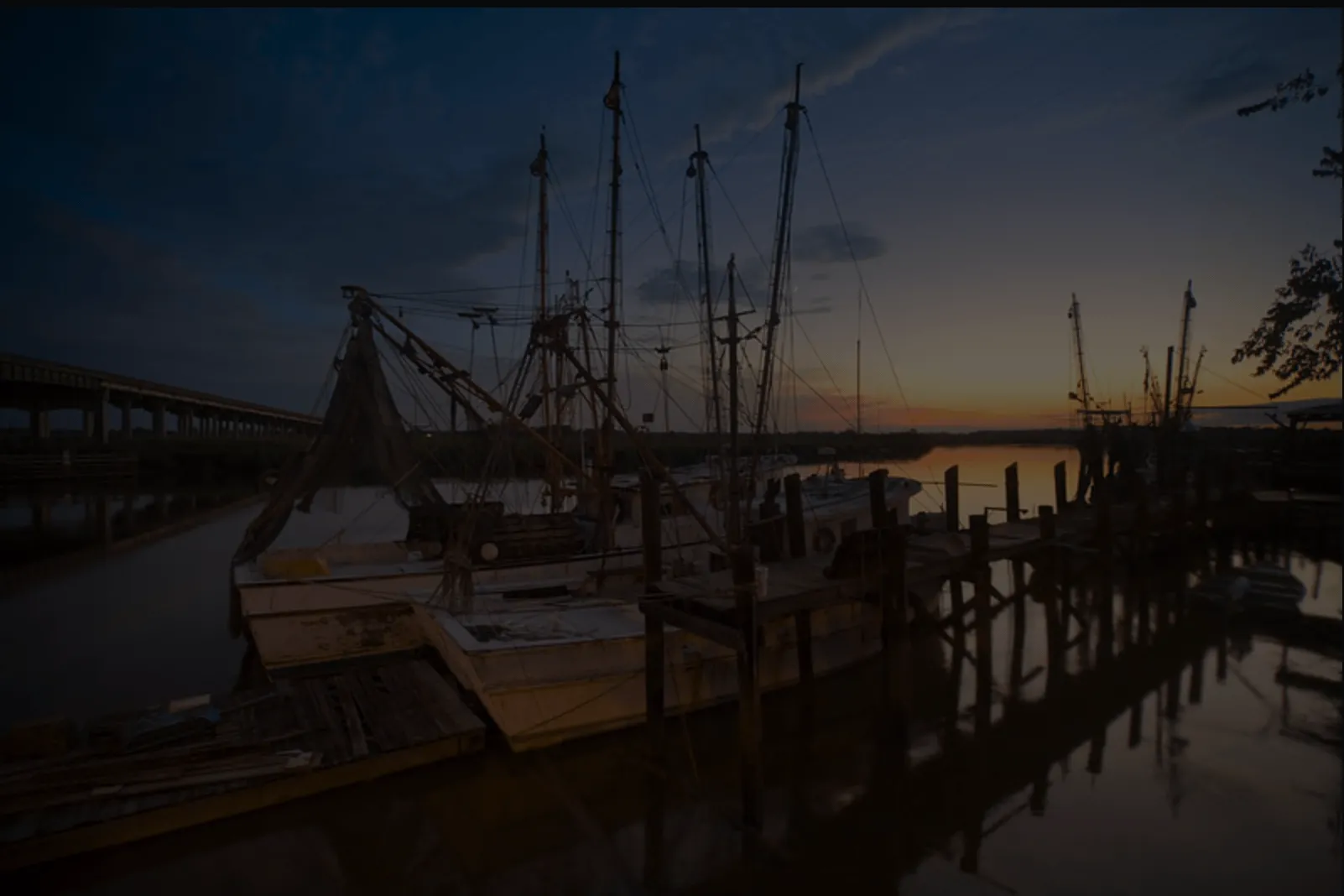 Fishing boats docked at sunset, with calm water and a bridge in the background.