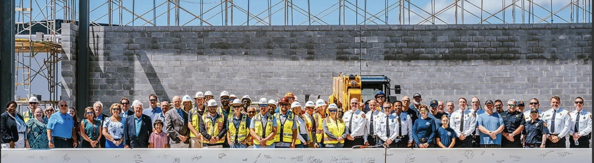 A large group of people in construction attire and formal wear stands at a building site.
