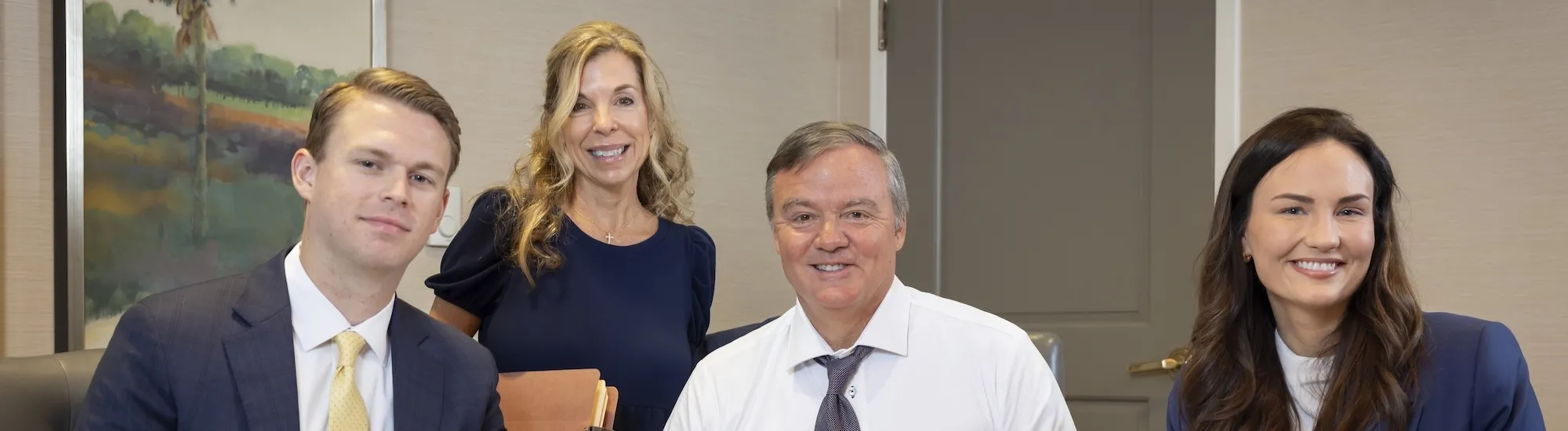 Four people in business attire smiling around a conference table.