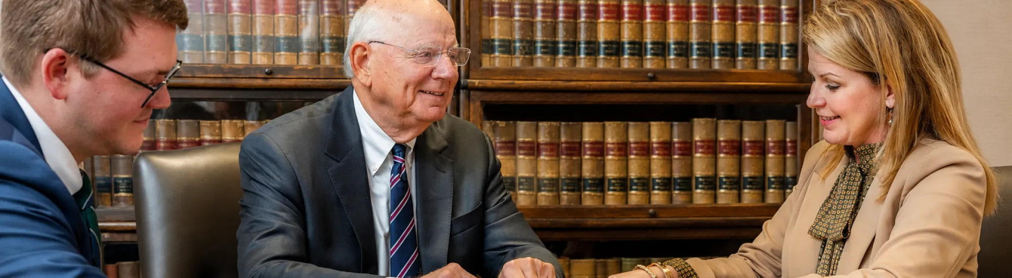 Three people discussing documents at a table in an office with law bookshelves.