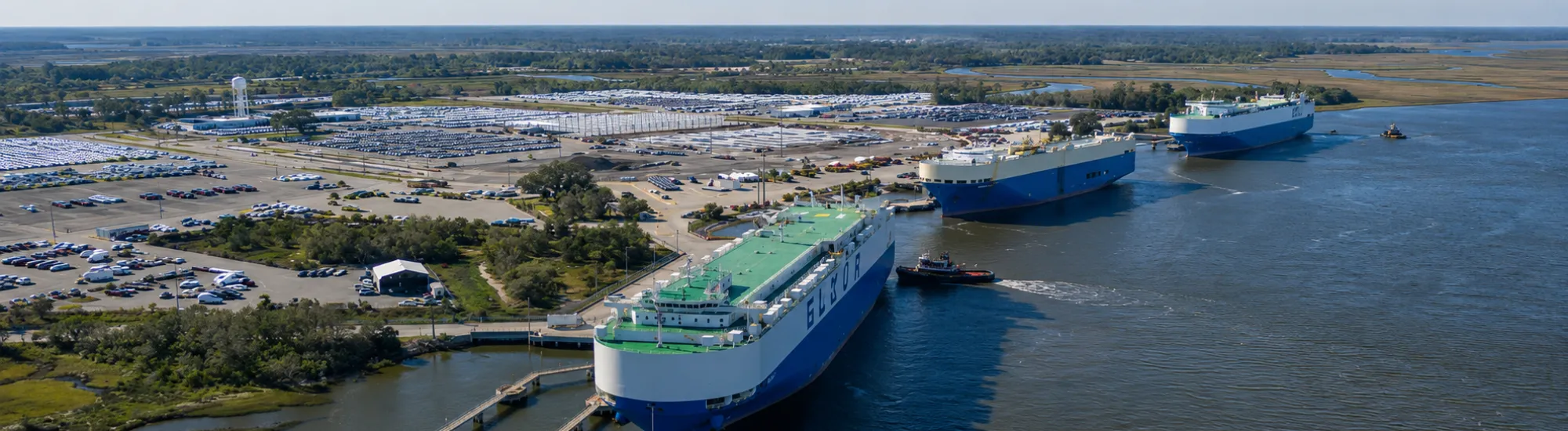 Docked cargo ships under a blue sky along a riverside industrial area.